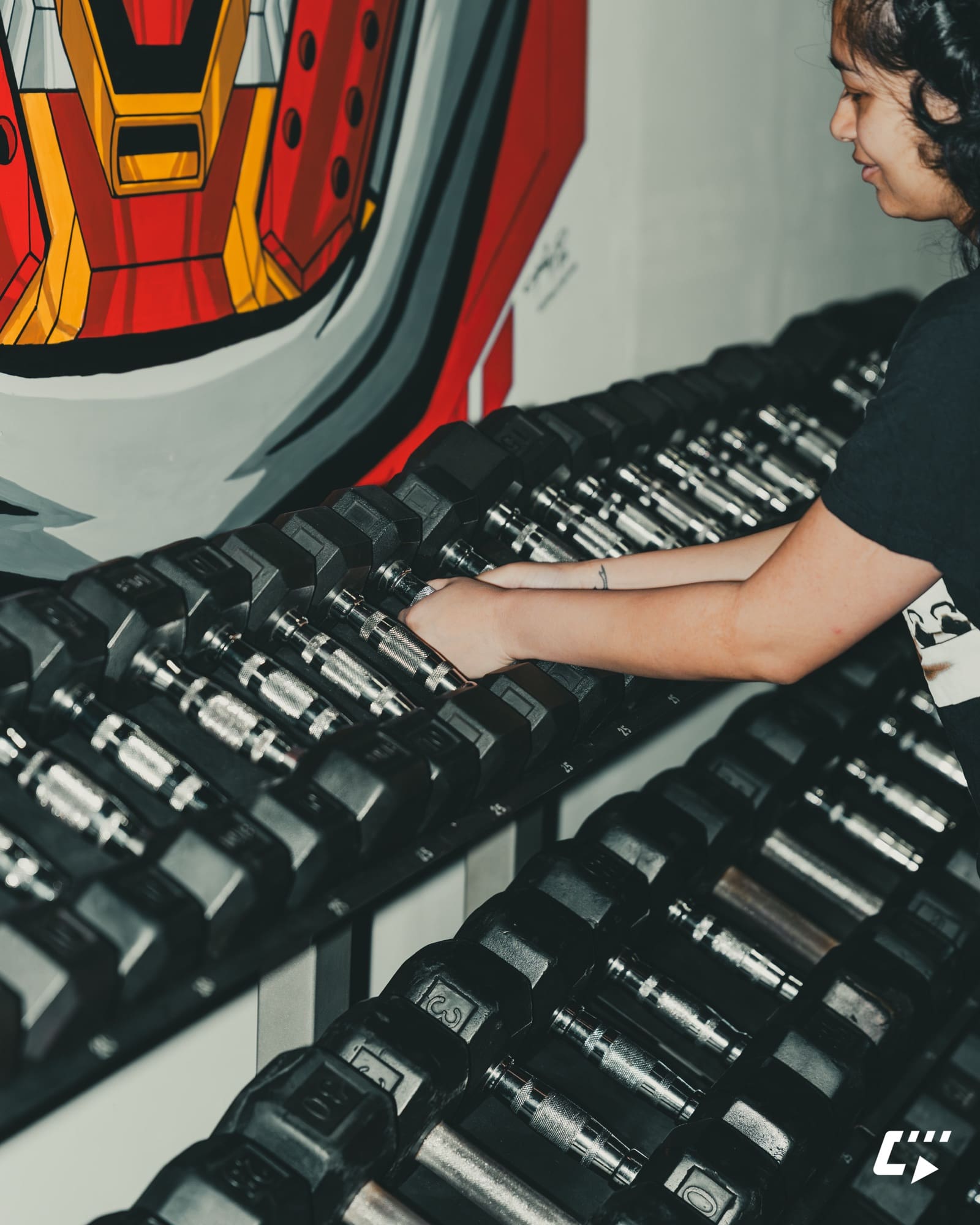 Member selecting dumbbells beside the HSC Gym mural